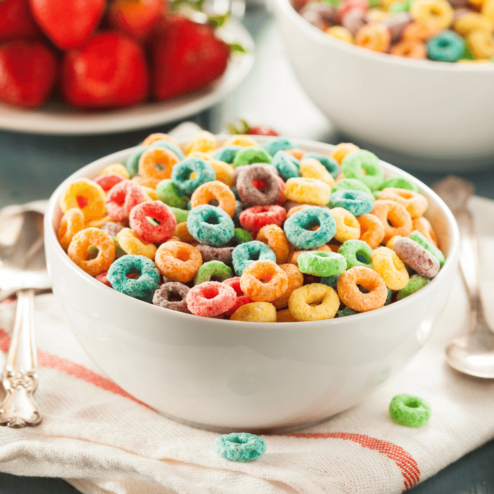 Fervor Candle Company Magic Cereal Room & Linen Spray scent inspiration photo. A big white bowl full of colorful Fruit Loops cereal on a cloth napkin with silver breakfast spoon.