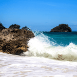 Under the Sea Snap Bar Soy Wax Melt Tart by Fervor Candle Company scent inspiration photo. White seafoam waves from a peaceful turquois ocean crashing against a large beach rock on a bright sunny day.